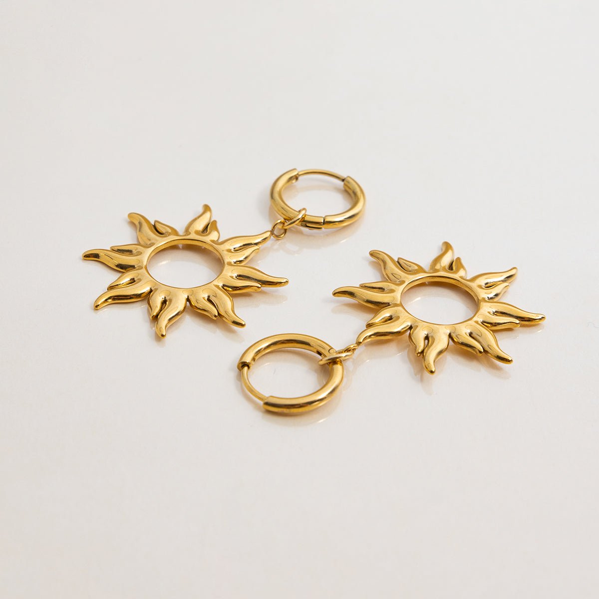 Gold sun-shaped earrings on a light gray background
