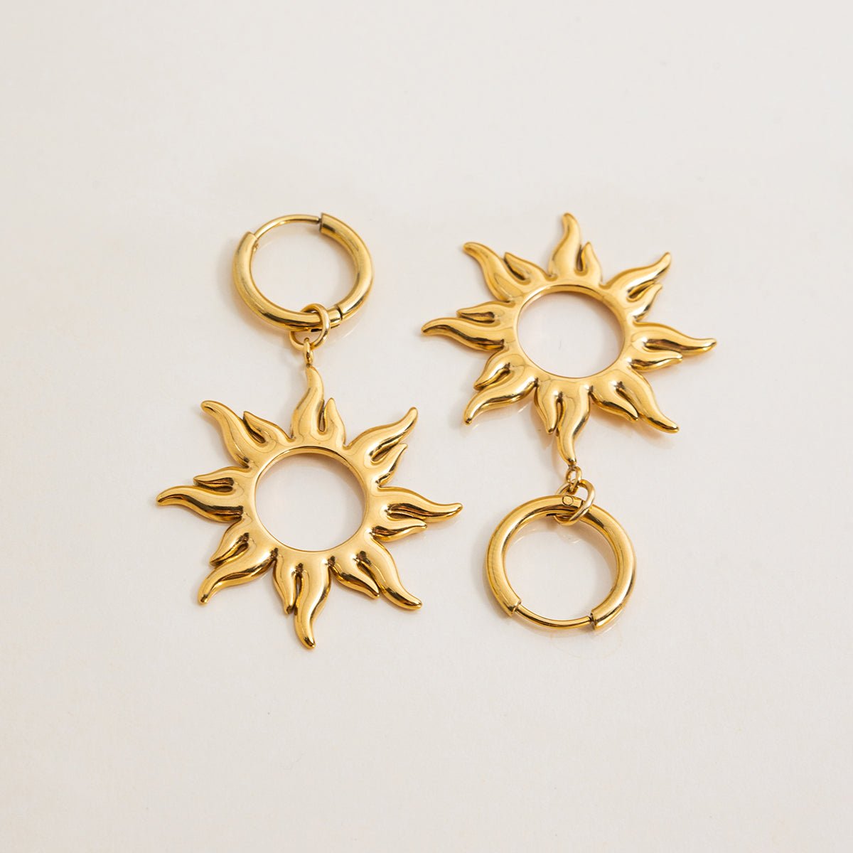Gold sun-shaped earrings on a light beige background