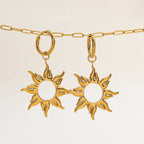 Gold sun-shaped earrings on a beige background