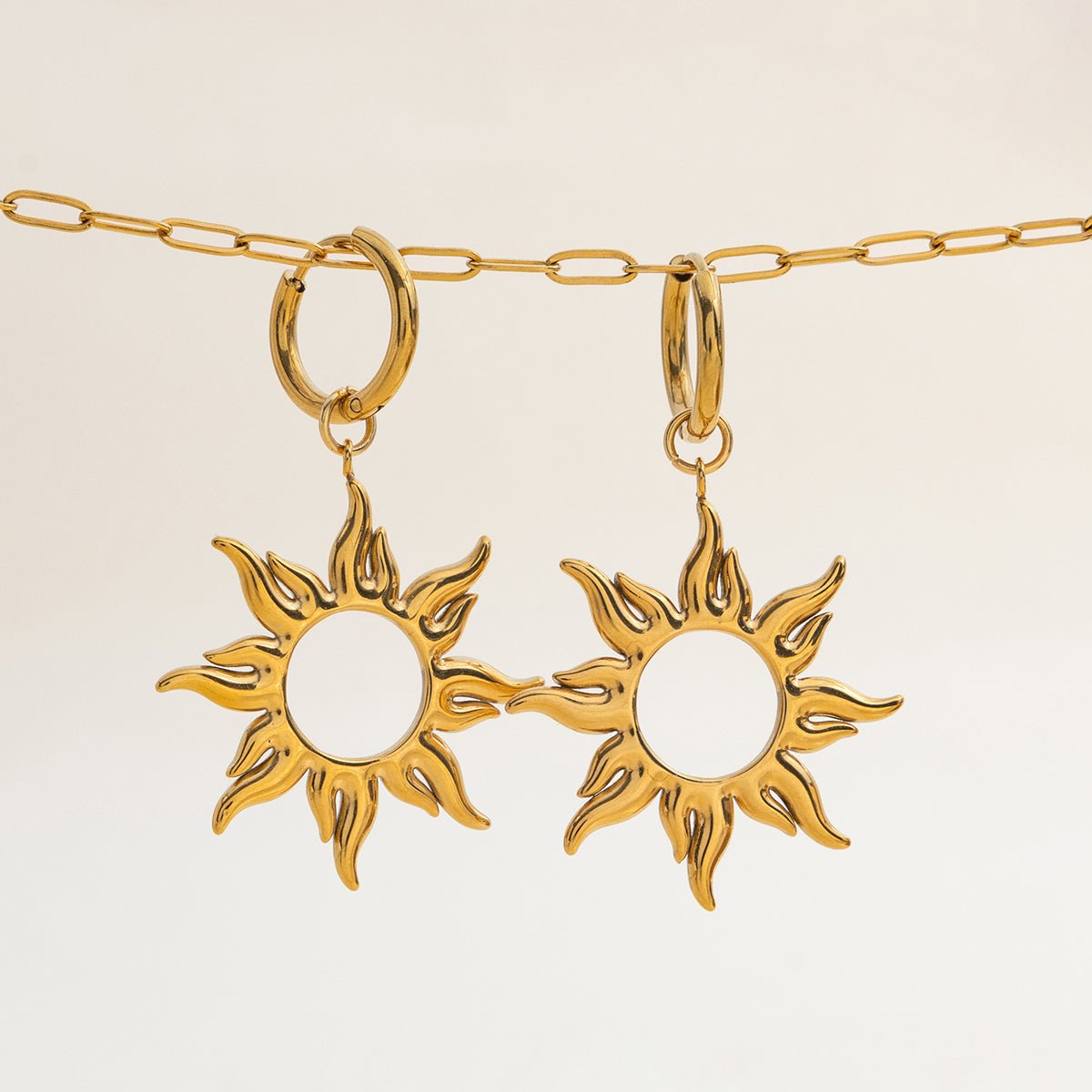 Gold sun-shaped earrings on a beige background