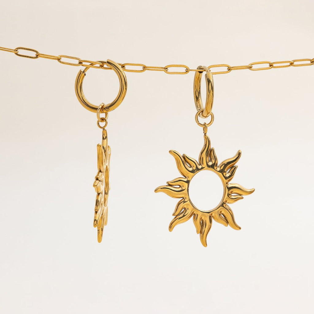 Gold necklace with a sun-shaped pendant and a leaf-shaped charm on a beige background