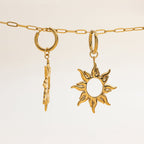 Gold necklace with a sun-shaped pendant and a leaf-shaped charm on a beige background