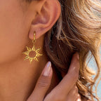 Gold sun-shaped earring worn on an ear with a close-up view.