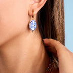 Close-up of a person wearing a blue and white patterned earring with a hand adjusting it.