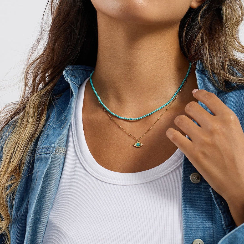 Woman wearing a turquoise beaded necklace and white tank top with a blue denim jacket.