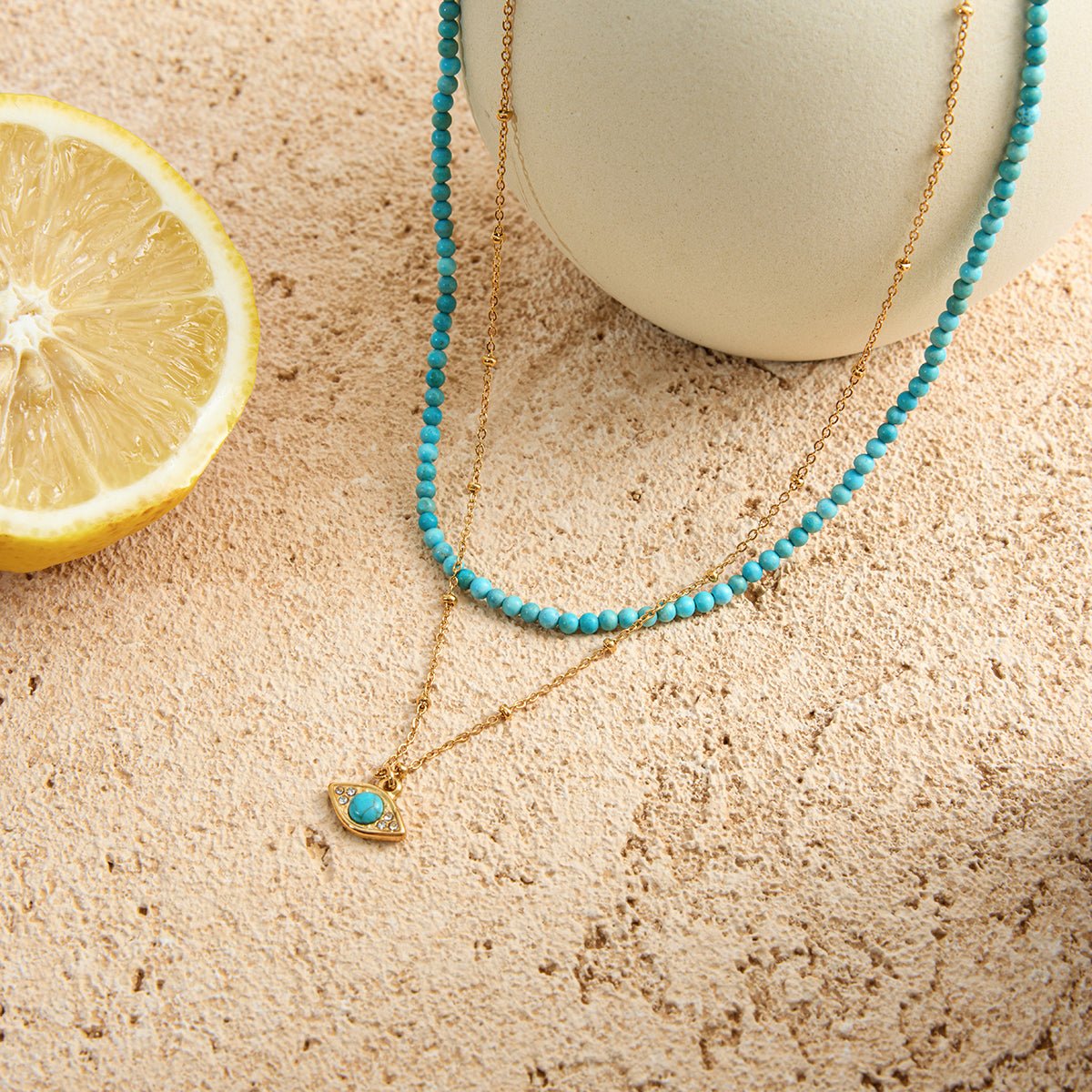 Turquoise beaded necklace with a heart pendant on a sandy surface next to a lemon slice.