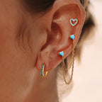 Close-up of an ear wearing gold earrings with turquoise stones.