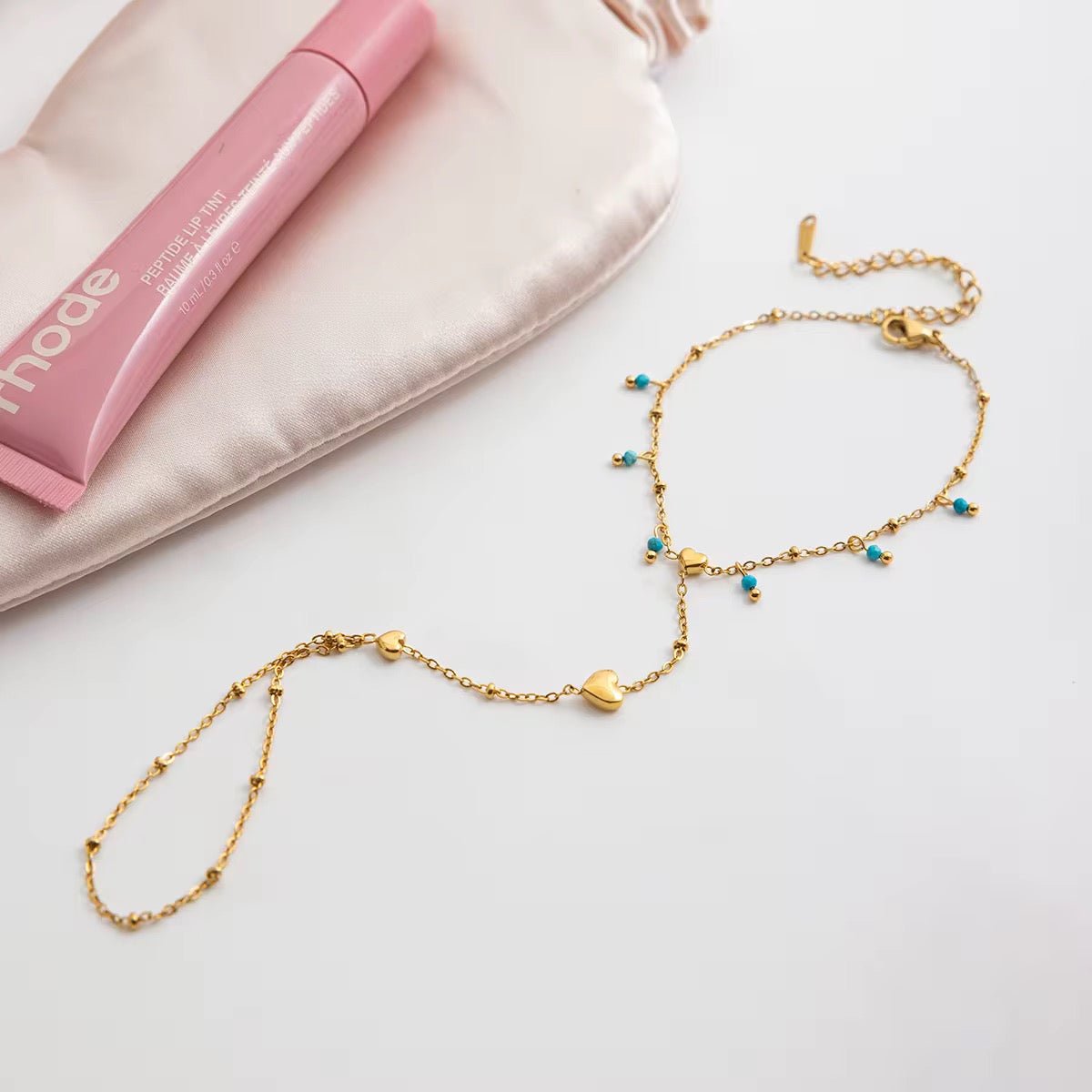 Gold necklace with blue beads on a white surface with pink makeup case in the background