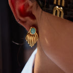 Gold earring with a green turquoise gemstone worn by a person.