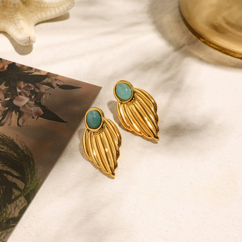 Gold earrings with turquoise stones on a textured surface