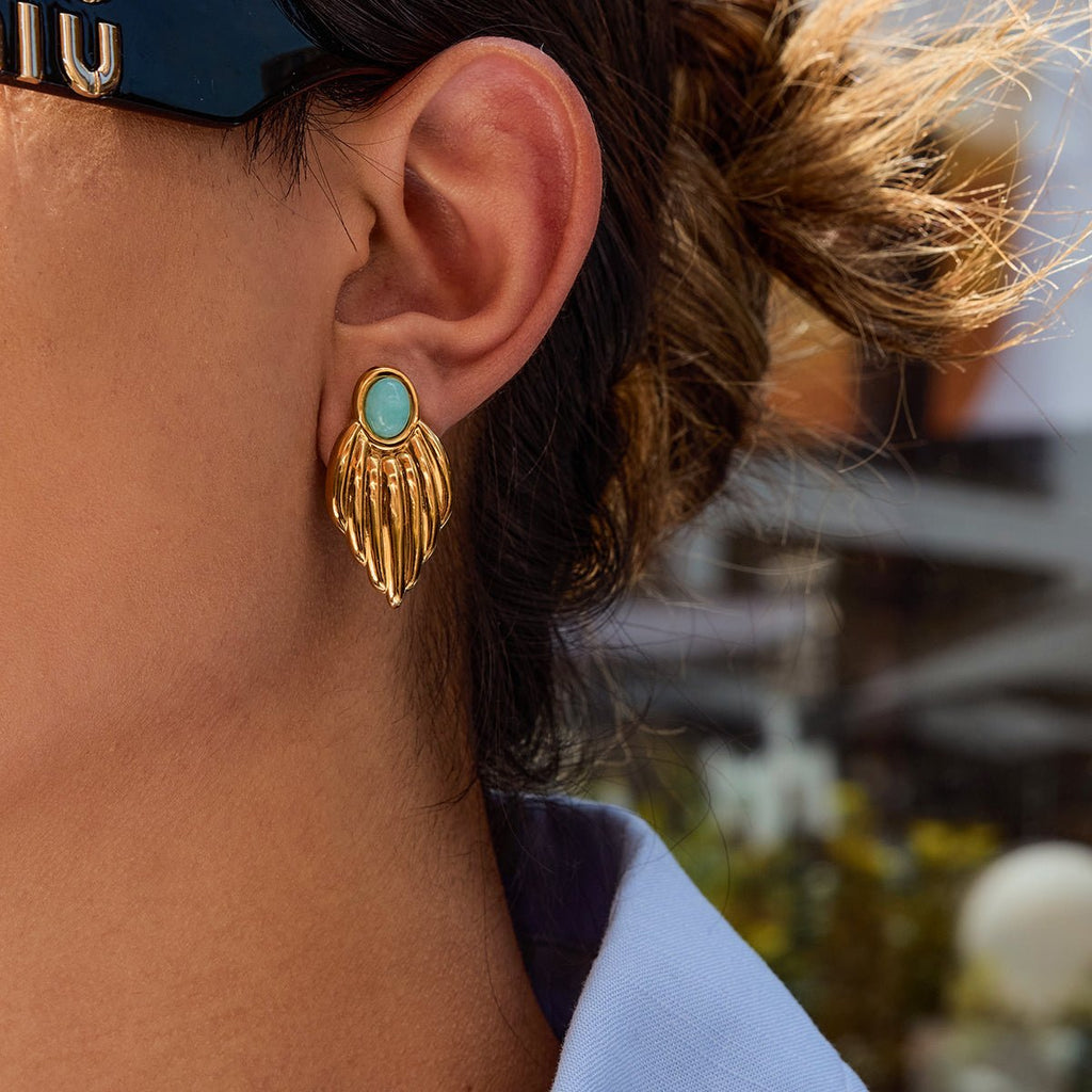 Close-up of a person wearing a gold earring with a turquoise stone, blurred background