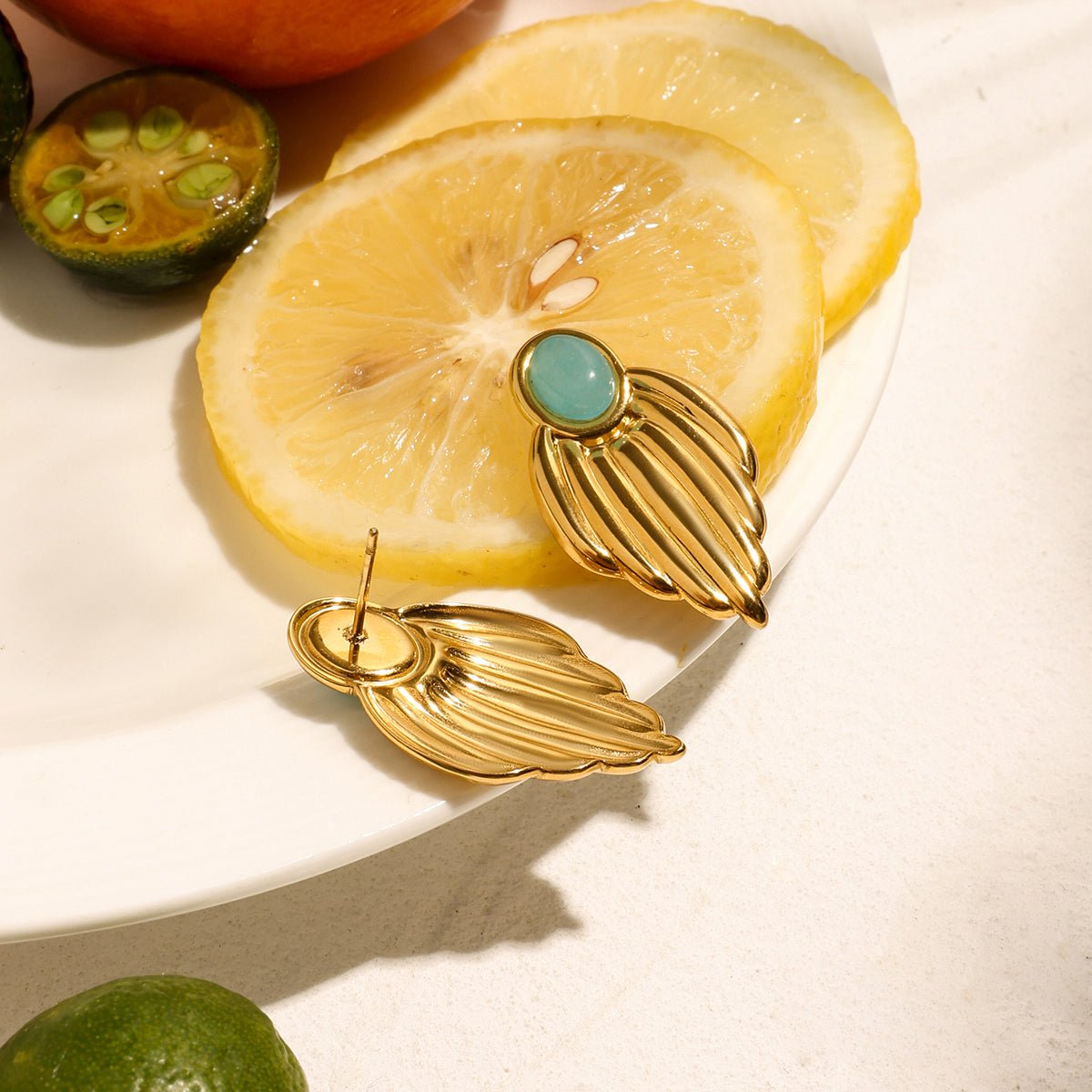 Gold earrings with a turquoise stone on a plate with lemon slices and limes.
