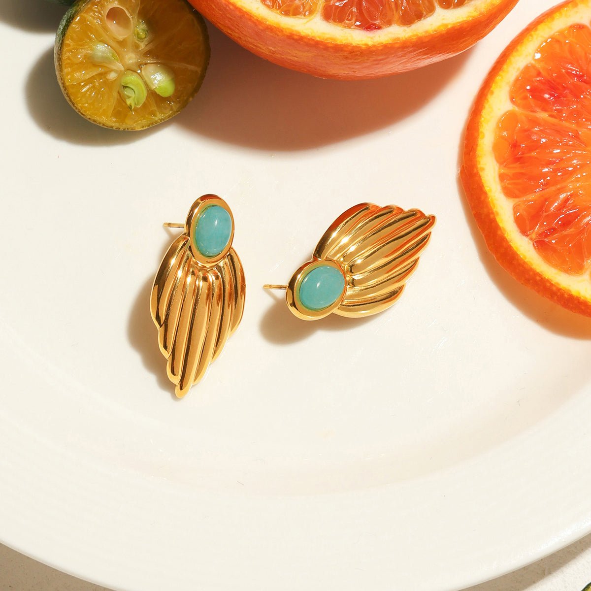Gold earrings with turquoise stones on a white surface with sliced oranges and limes.