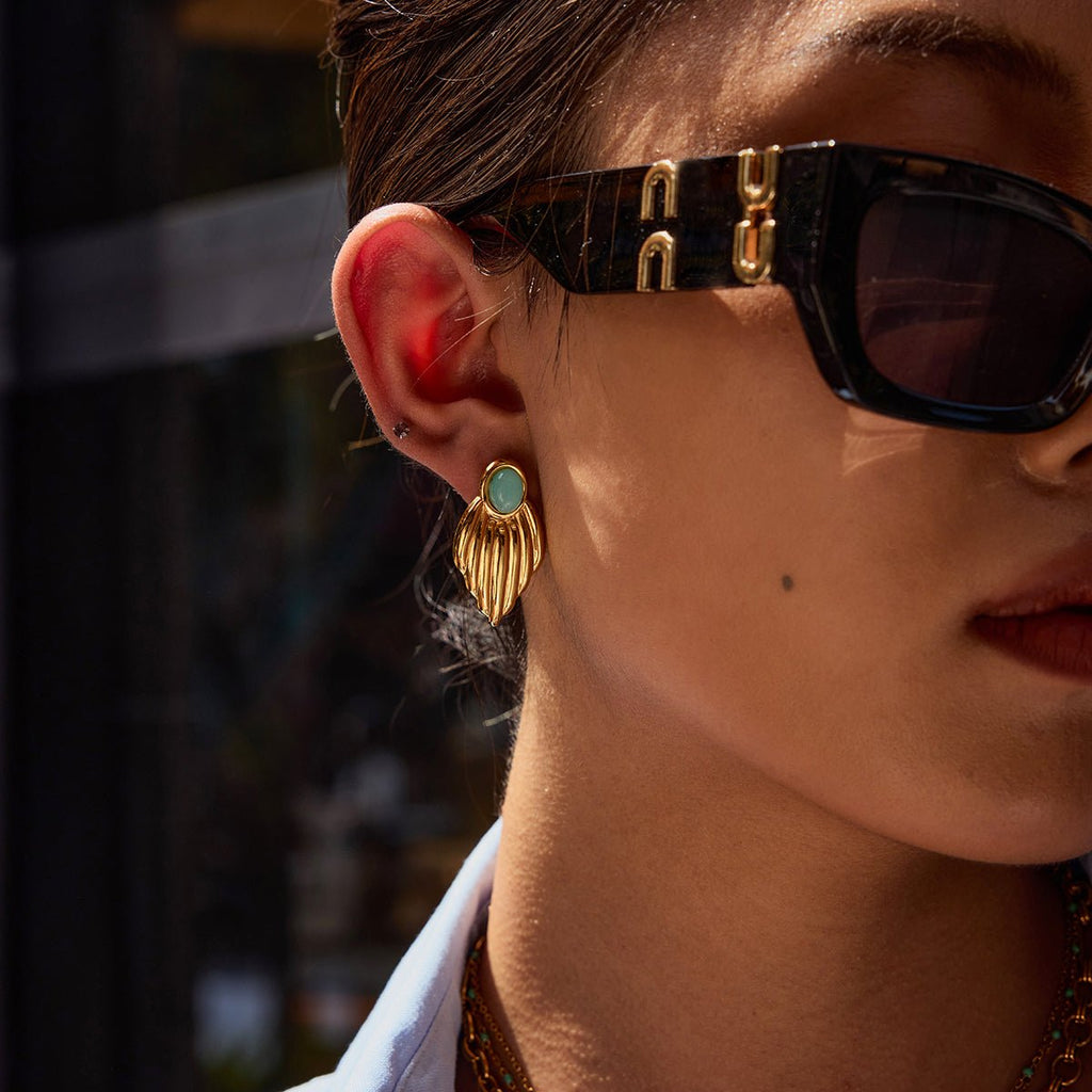 Close-up of a person wearing sunglasses with gold and turquoise earrings.