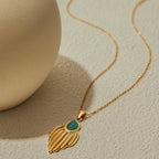 Gold necklace with a leaf-shaped pendant and green gemstone on a beige background