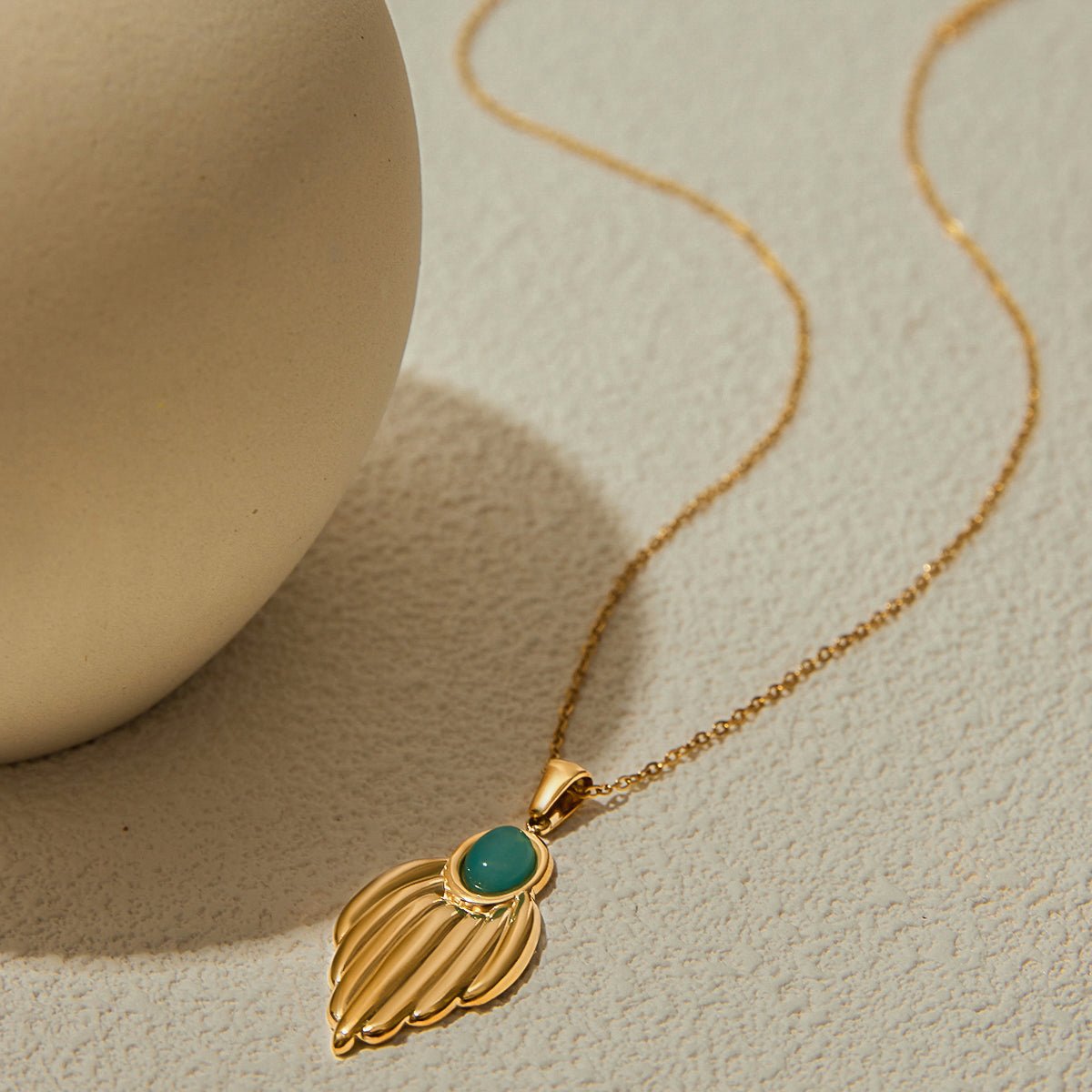 Gold necklace with a leaf-shaped pendant and green gemstone on a beige background