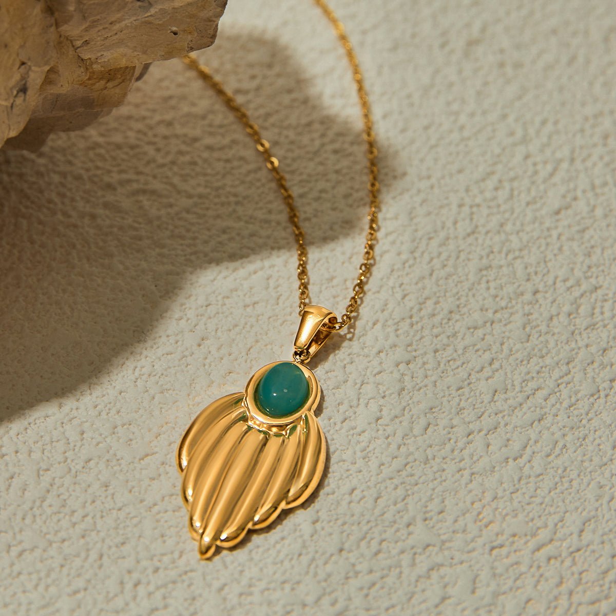 Gold necklace with a green pendant on a textured beige background