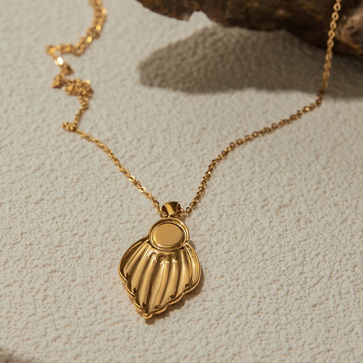 Gold necklace with a detailed pendant on a textured beige surface
