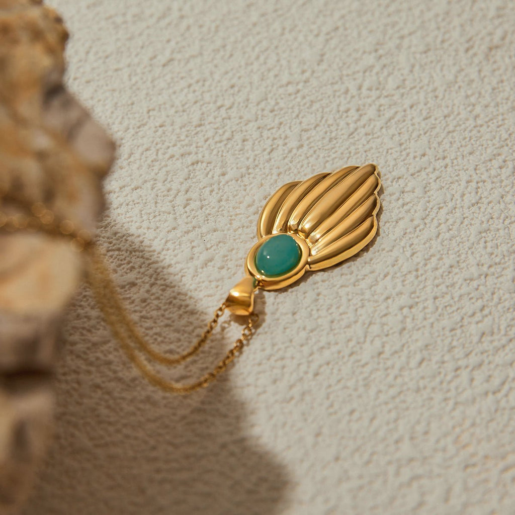 Gold brooch with a green gemstone on a textured beige background