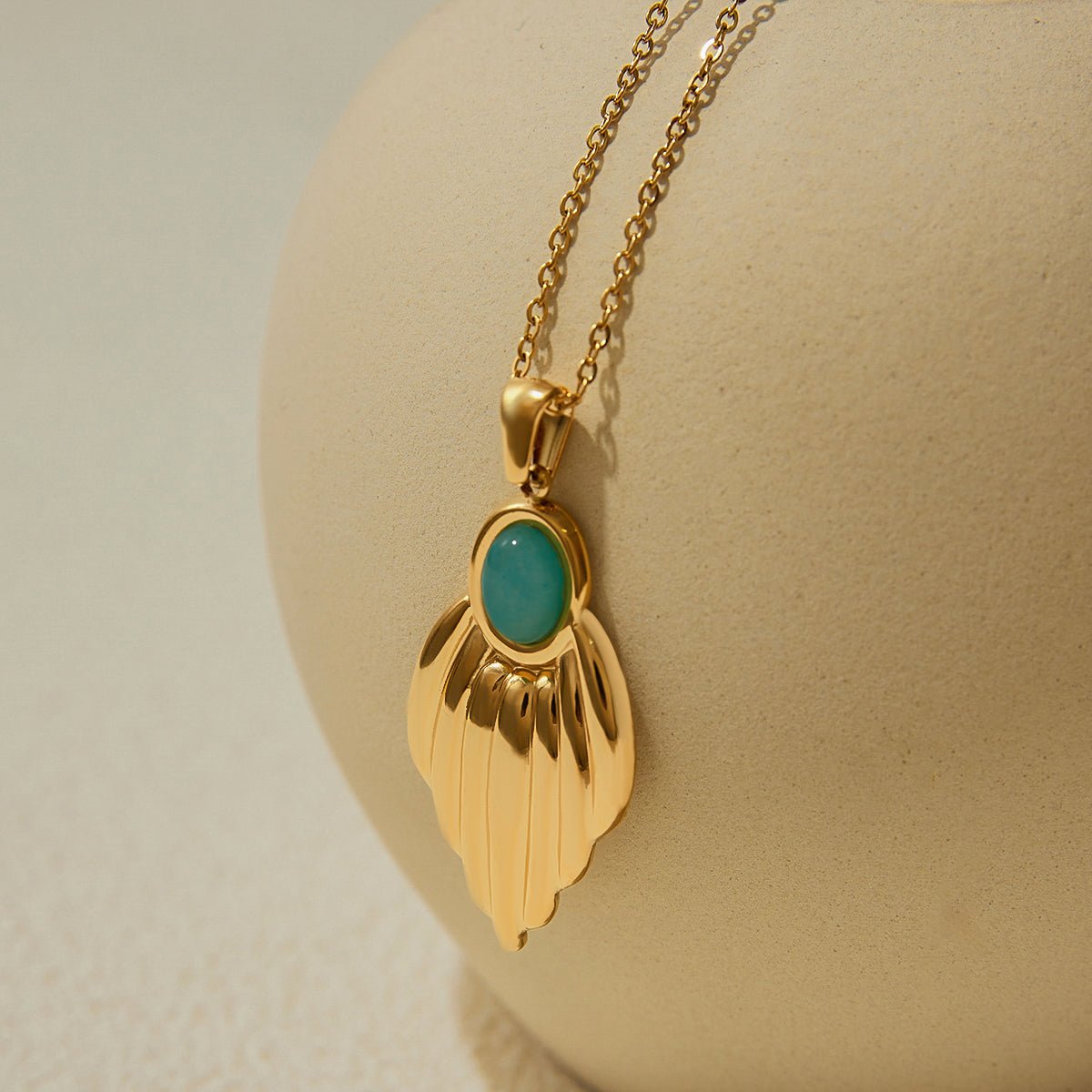 Gold necklace with a green pendant on a beige background