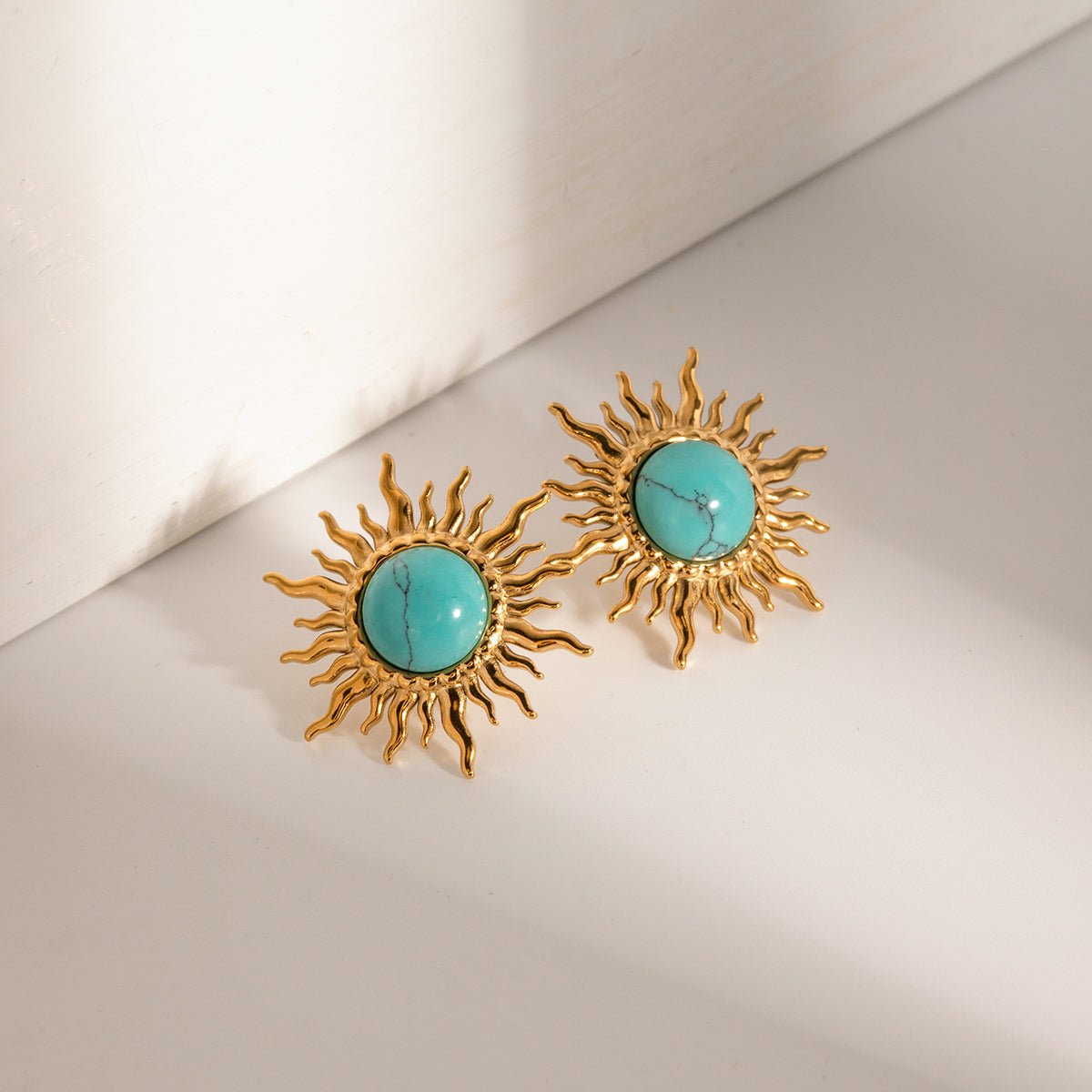 Gold sun-shaped earrings with turquoise stones on a light background