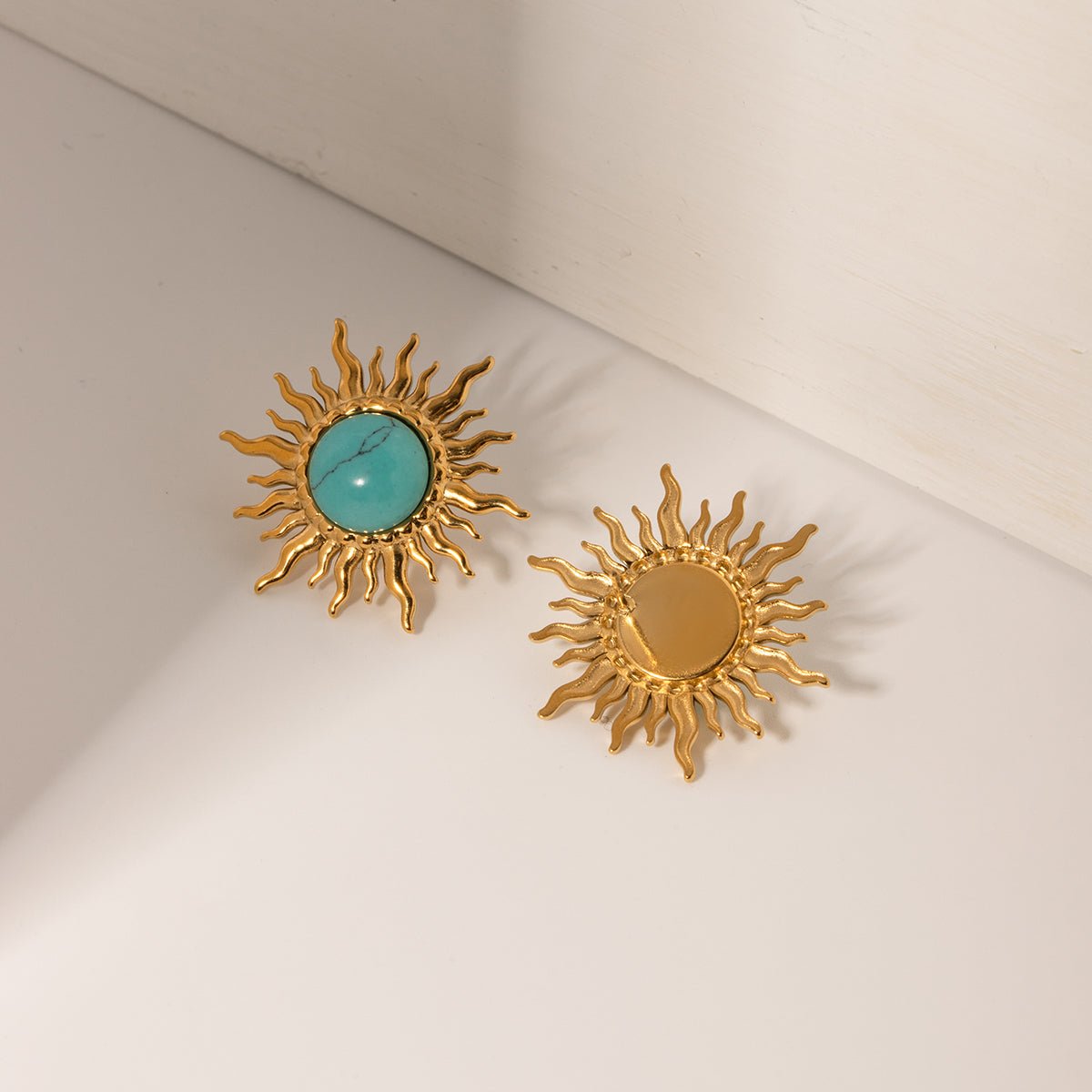 Gold sun-shaped earrings with turquoise center on a beige background