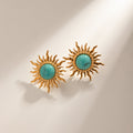Gold sun-shaped earrings with turquoise centers on a beige background