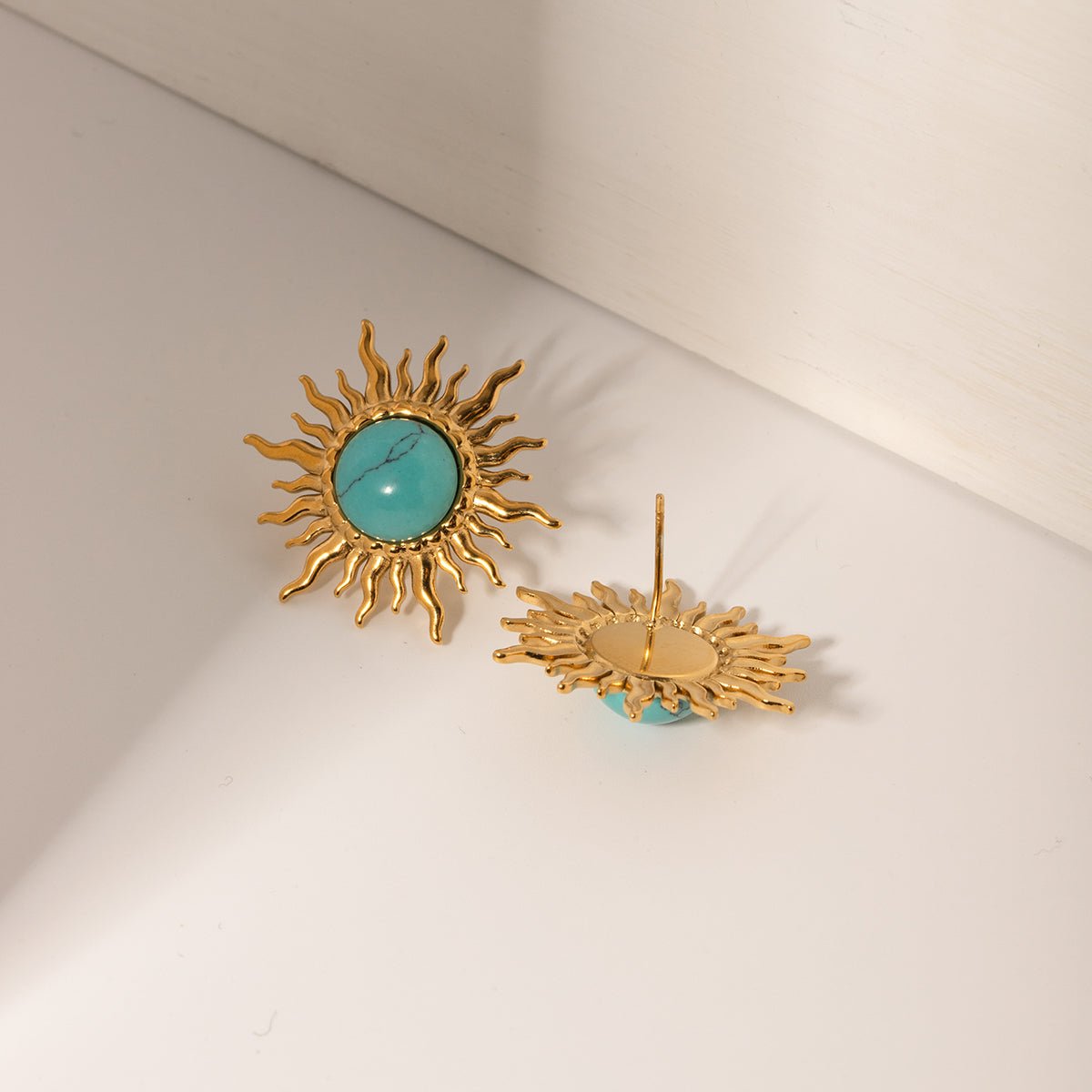 Gold sun-shaped earrings with turquoise centers on a light beige background