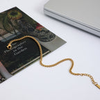 Gold chain necklace on a book with a laptop in the background