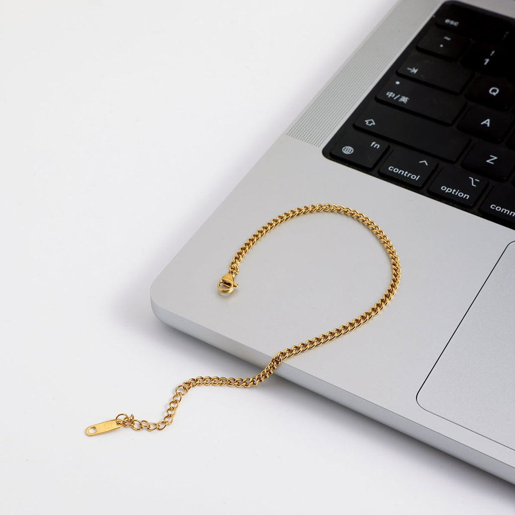 Unisex gold curb chain bracelet with adjustable clasp on a laptop keyboard