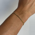 Gold chain bracelet on a wrist against a neutral background