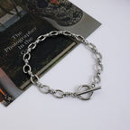 Silver chain bracelet on a white surface with a book and decorative item in the background