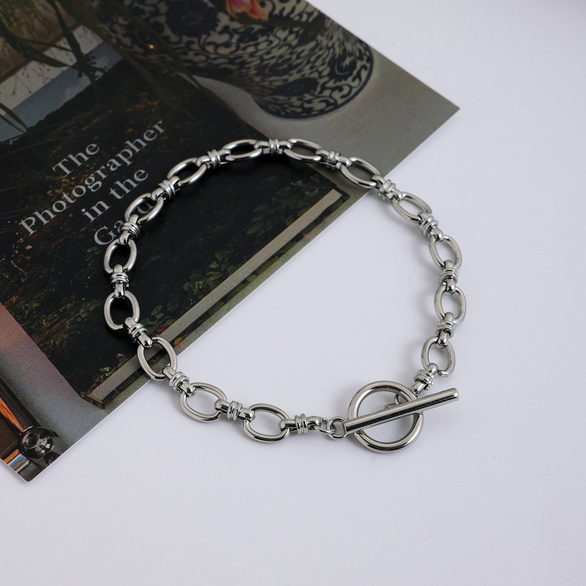 Silver chain bracelet on a white surface with a book and decorative item in the background