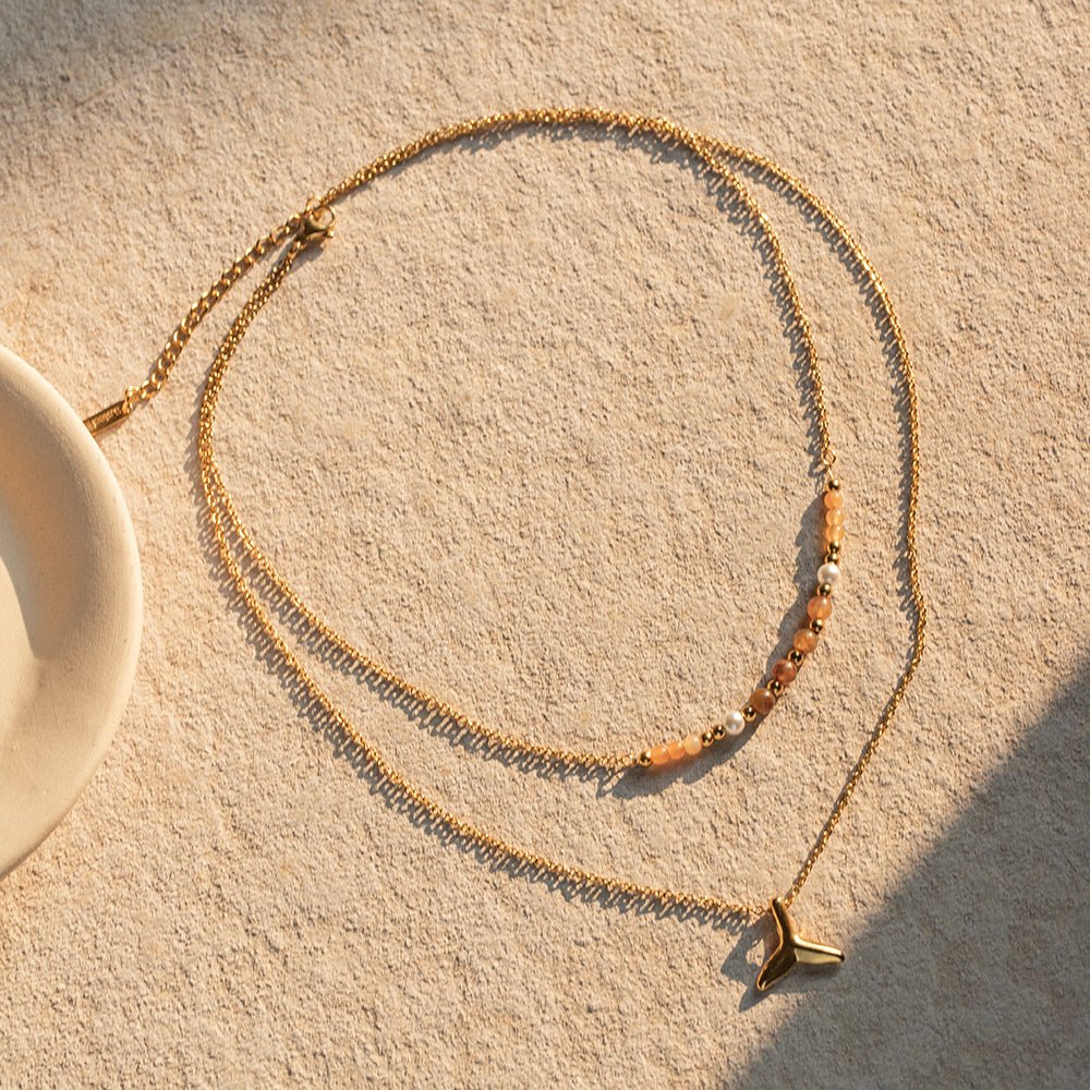Gold necklace with a pendant on a textured beige surface