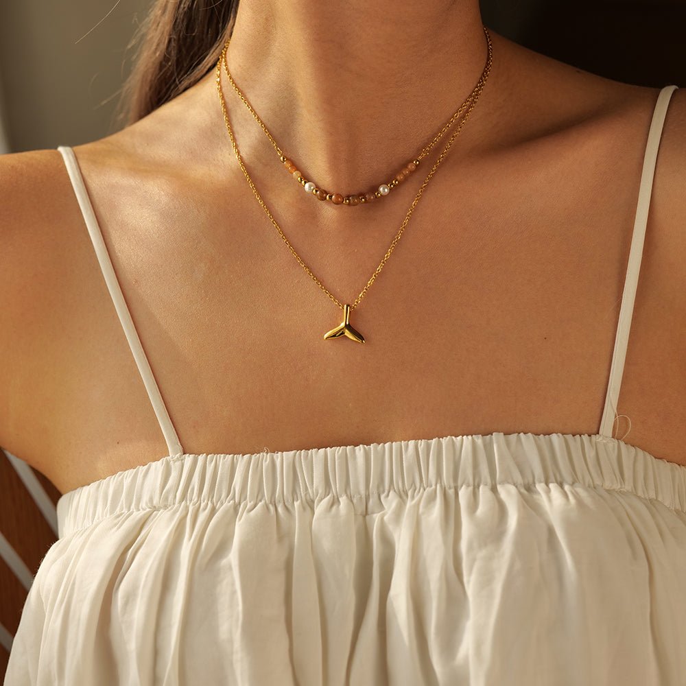 Close-up of a person wearing a gold necklace with a mermaid tail pendant.